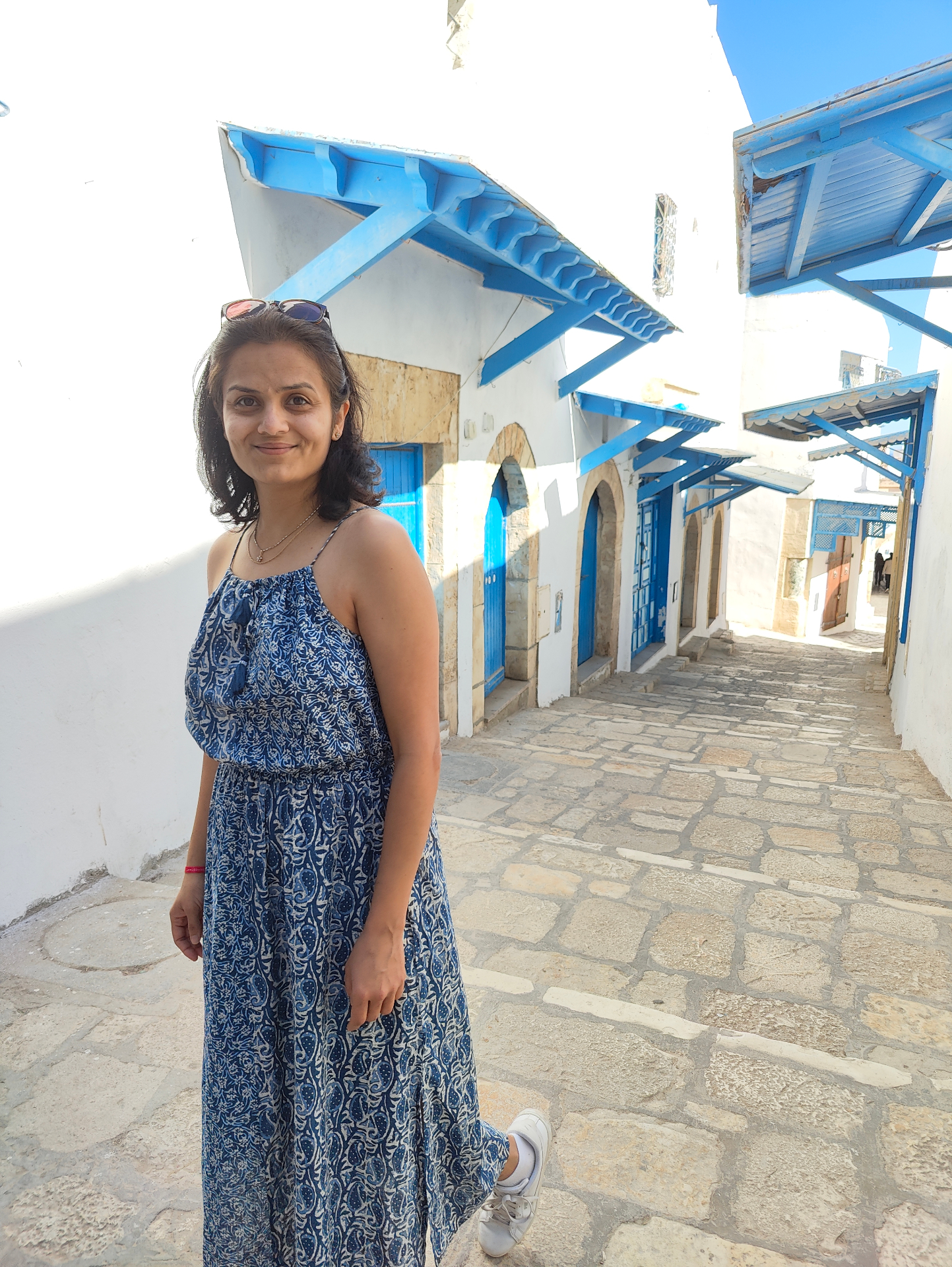 Neha Mehta standing in a sunlit blue-and-white alley